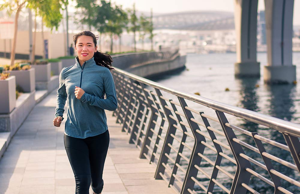 A woman runs on a path along a city waterfront.