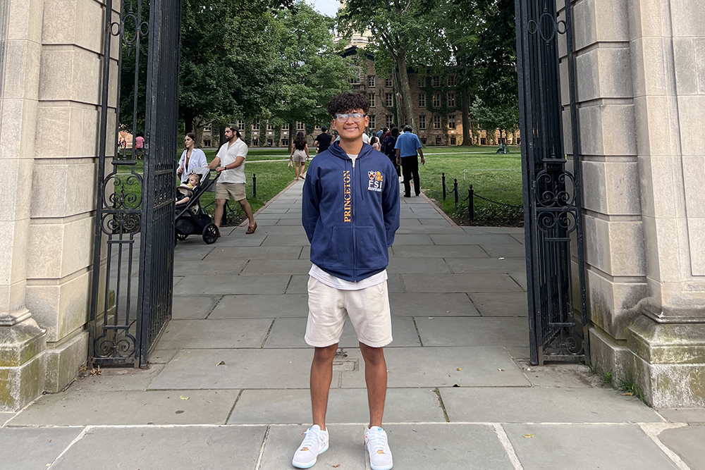 Alexis Cruz stands on the Princeton campus in tan shorts and a blue zip-up hoodie