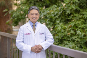 Dr. Fumito Ito stands outside in a white medical coat and smiles.