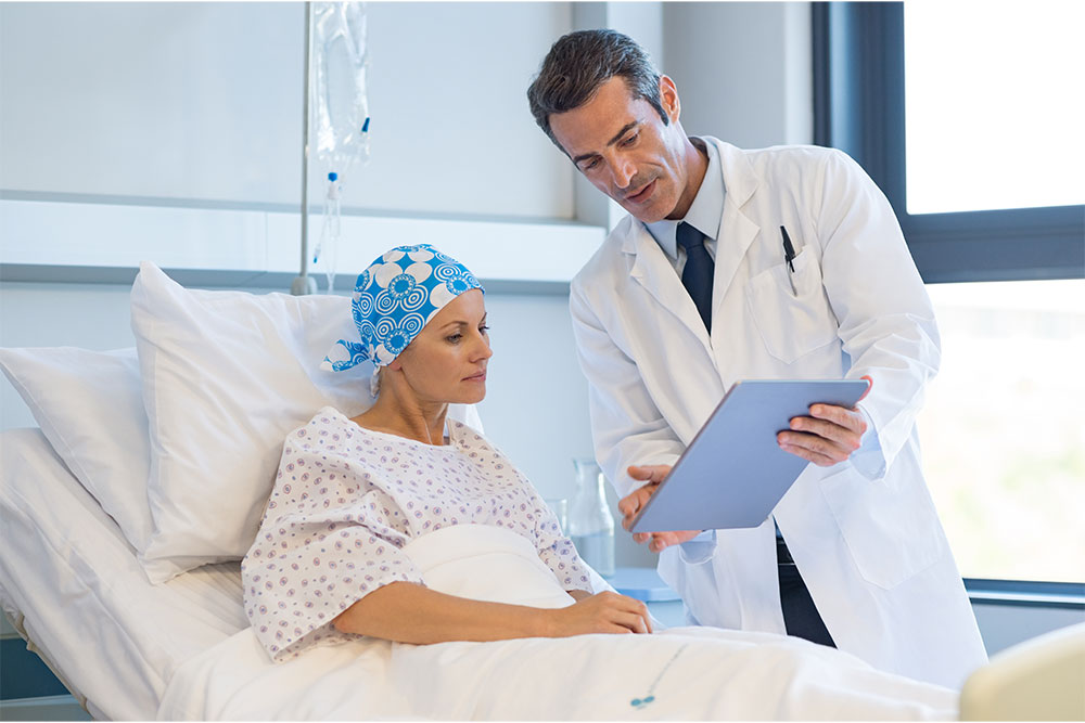 A male doctor shows a cancer patient results as they lie in bed.